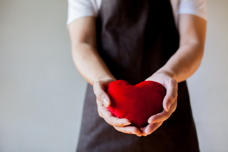 Servicing man in apron holding heart - customer relationship and service minded business concept.の写真素材