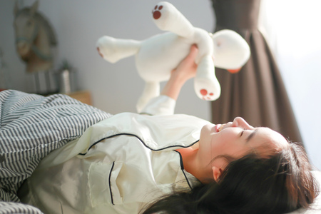 Smiling Asian woman lying down on bed and waking up happily in bedroom -selective focusの写真素材