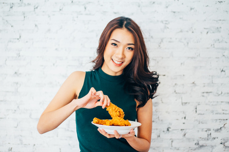 Attractive Asian woman eating fried chicken drumstick over white brick backgroundの写真素材