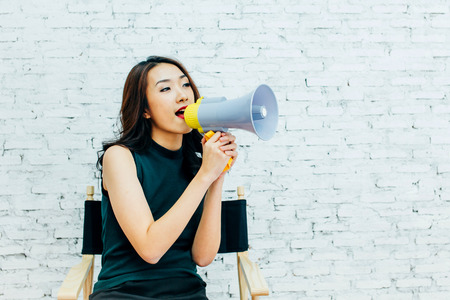 Asian business woman shouting with megaphone over white bricks wall backgroundの写真素材