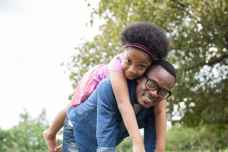 African American father and daughter playing and carrying on back in green park sceneの写真素材