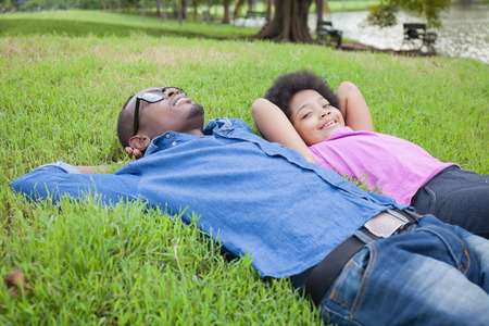 African American Young man and little kid relaxing and looking at clouds on green parkの写真素材