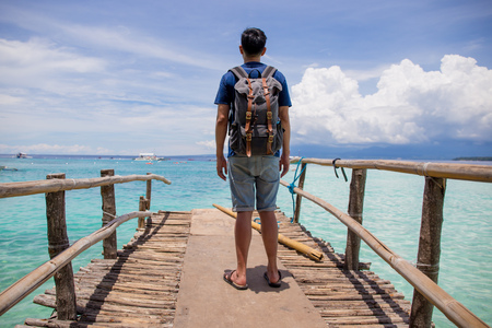 Traveling man with backpack looking out towards the beautiful and crystal clear ocean sea in summerの写真素材