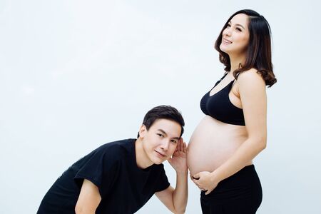 Expectant husband listening to pregnant woman wife over isolated white backgroundの写真素材