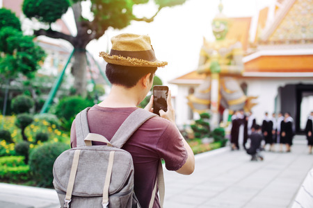 Young Asian traveling backpacker taking photos with smartphone in Wat Arun in Bangkok, Thailandの写真素材
