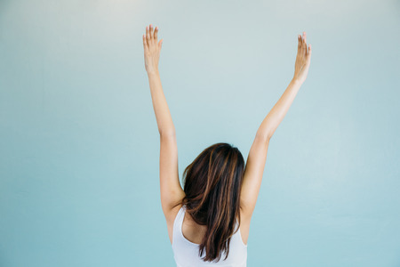 Back of beautiful young woman with arms raised over blue green backgroundの写真素材