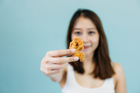 Asian woman with mouth opened eating eat deep fried chicken legs drumstick (Focus on foreground)の写真素材