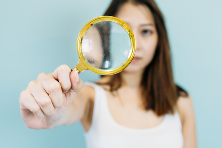 Young Asian woman with magnifying glass isolated on a blue pastel backgroundの写真素材