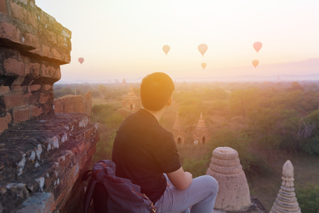 Silhouette of young male backpacker sitting and watching hot air balloon travel destinations in Bagan, Myanmarの写真素材