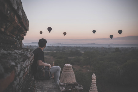 Silhouette of young male backpacker sitting and watching hot air balloon travel destinations in Bagan, Myanmarの写真素材