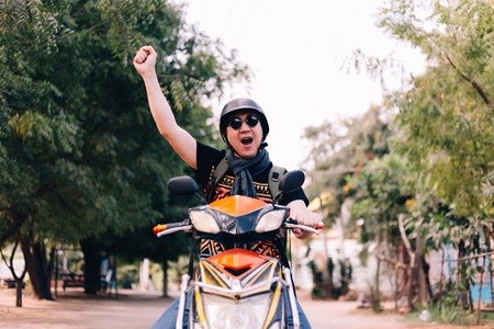 Young man in sunglasses and helmet riding motorcycle raising hands up as winner and successの写真素材