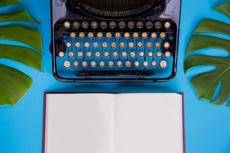Open book with blank paper pages decorated with typewriter and leaves over bright blue background - with copy spaceの写真素材