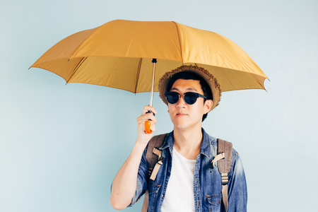 Young Asian tourist holding umbrella isolated over pastel blue background. Alone and Looking for partner to travelの写真素材