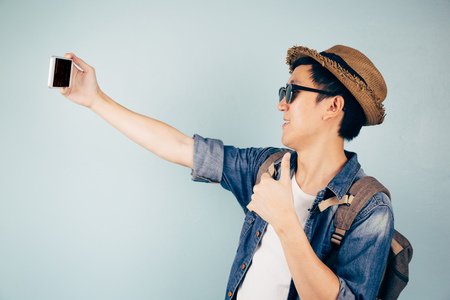 Young Asian tourist smiling and taking a selfie isolated over pastel blue backgroundの写真素材