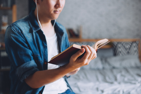 Young man reading book in living cozy roomの写真素材