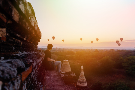 Silhouette of young male backpacker sitting and watching hot air balloon travel destinations in Bagan, Myanmarの写真素材