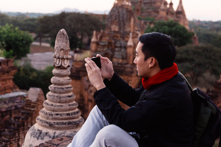Young man taking a photo with mobile phone in temple stupa architecture scenery