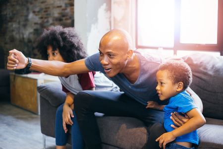 Happy African American family of three watching tv and cheering sport games on sofa at homeの写真素材