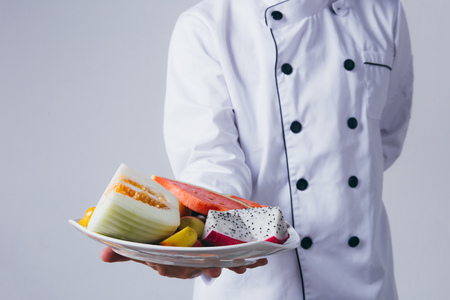 Chef presenting a plate of fruit slices isolated over white backgroundの写真素材