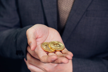 Close-up of businessman showing and holding bitcoin sign of coin - indicating crypto currency and future of digital financial banking tradeの写真素材