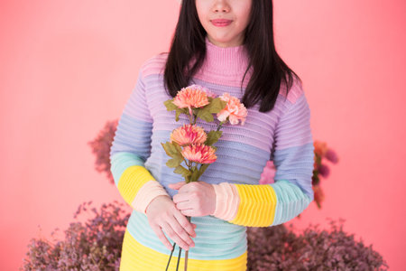 Close-up of Cheerful young woman holding bunch of flowers in colorful sweater isolated over pink backgroundの写真素材