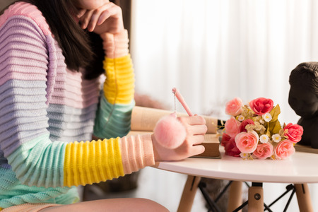 Close-up of Young woman in colorful fashionable sweater writing a diary and drawing in the bookの写真素材
