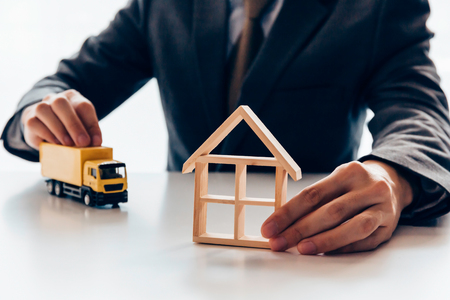 Businessman holding a miniature of house and delivery toy truck, indicating the concept of direct delivery to house, moving relocation and freight service.の写真素材
