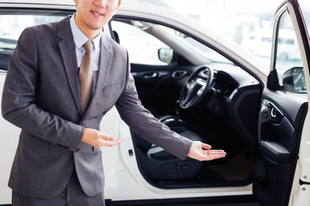 Young chauffeur in business suit welcoming rich and wealthy client on board - rich lifestyle taxi car transportation conceptの写真素材