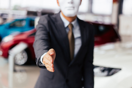 Dishonest and evil salesman in business suit in car dealership company handshaking welcome customers to exploit and deceive customers - fraud and bad quality service in business conceptの写真素材