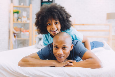 African American family of two, child sitting on father's back at homeの写真素材