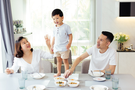 Asian family watching their kid as he is determined and proud to finally stand on the dining tableの写真素材