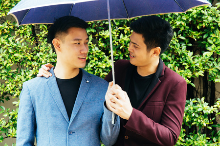 Gay couple holding umbrella and hands together. Asian homosexual men walking in the rainの写真素材