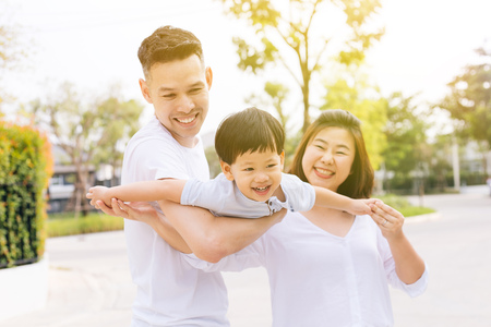 Asian family having fun and carrying a child in public parkの写真素材