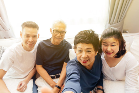 Asian family with adult children and senior parents taking selfie and sitting on a sofa at home....
