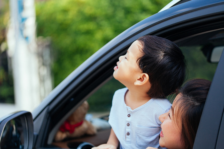 Happy Asian family is looking up in the sky and travelling on the road trip, going for a drive for vacationの写真素材