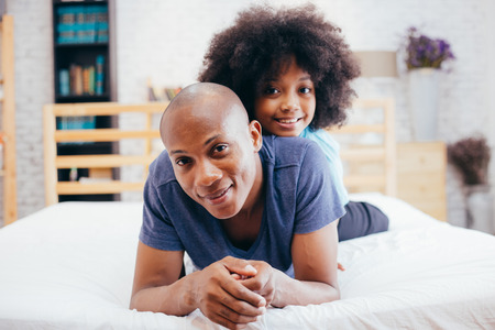 African American family of two, child sitting on father's back at home (focus on father)の写真素材