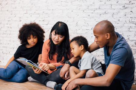 African American parents reading a fairy tale fable story for kids at home. Happy family sitting on the floor indoorsの写真素材