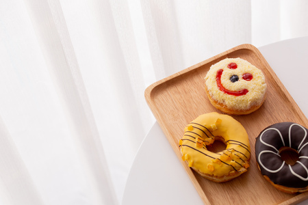 Close up of colorful and sweet donuts and one smiley face donut  near windowsの写真素材