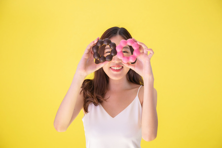 Attractive Asian woman holding two donuts with cute smiling expression over yellow backgroundの写真素材