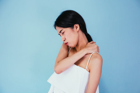 Young Asian woman having chronic neck and shoulder pain isolated over blue background - Healthcare...