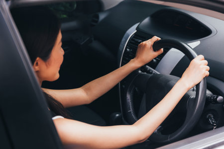 Rear view of young attractive Asian woman in casual wear looking at the road and driving a car
