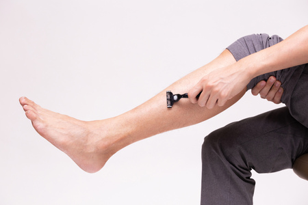 Part of human legs going to shave and remove leg hair with shaving razor in white isolated backgroundの写真素材
