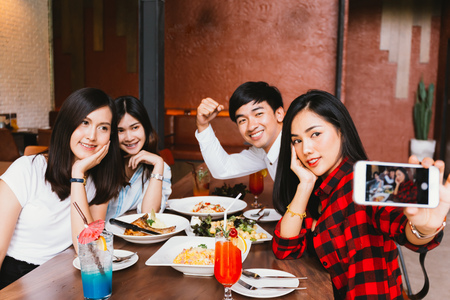 Group of Happy Asian male and female friends taking a selfie photo and having a social toast together in restaurant