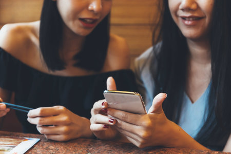 Two young attractive Asian women using a mobile phone together at restaurant with happiness and joy