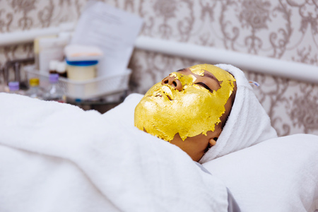 Young woman getting 24 karat gold facial treatment at the beauty clinic. The treatment of using real gold for youthful skinの写真素材
