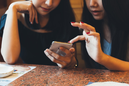 Two young attractive Asian women using a mobile phone together at restaurant with happiness and joyの写真素材