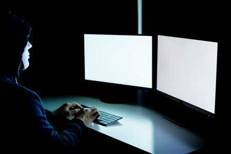 Anonymous and masked hacker using computer with isolated white monitor screen to insert any text,...