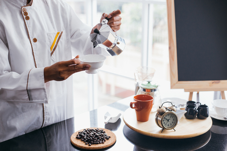 Young barista pouring coffee into a cup at cafe restaurant with happinessの写真素材