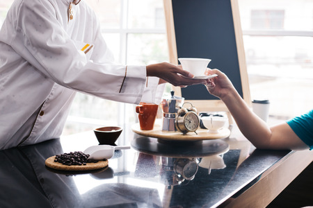 Young Asian female barista making and giving coffee to male customer. Business man receiving coffee at cafe restaurantの写真素材