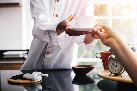 Young Asian female barista making and giving coffee to male customer. Business man receiving coffee at cafe restaurantの写真素材